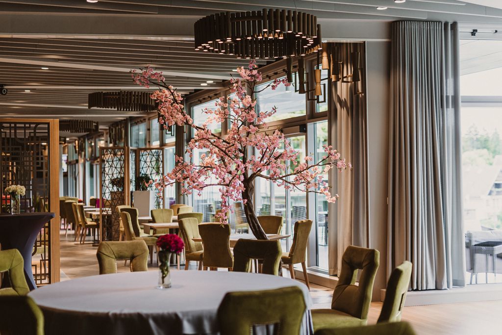 Elegant hotel restaurant with a round table, green upholstered chairs, and a pink cherry-blossom centerpiece.